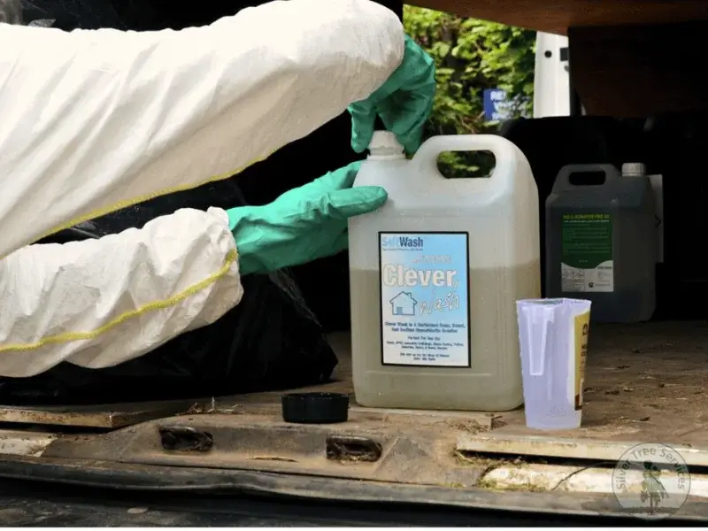 Man in a chemical spray suit screwing the cap onto a bottle of soft washing chemicals